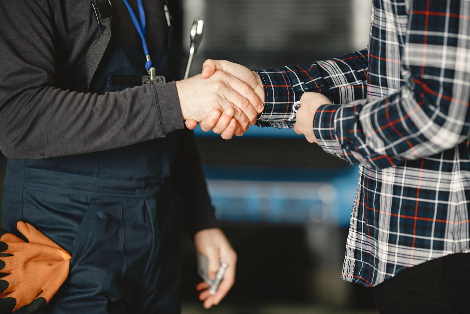 A tradesperson in work overalls shaking hands with a homeowner in a plaid shirt