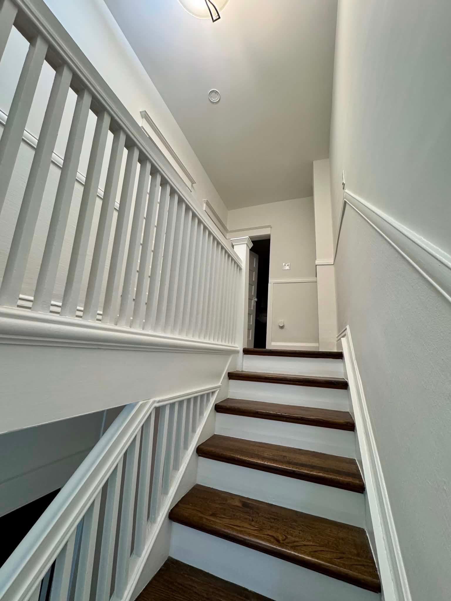 A clean, finished staircase in an older Toronto home with light-painted walls and trim and freshly stained wood treads